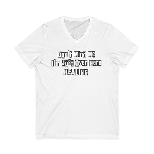 White Johny-T V-neck T-shirt with the printed inspirational text “Don’t Mind Me I’m Just Over Here Healing” displayed flat on a plain background.