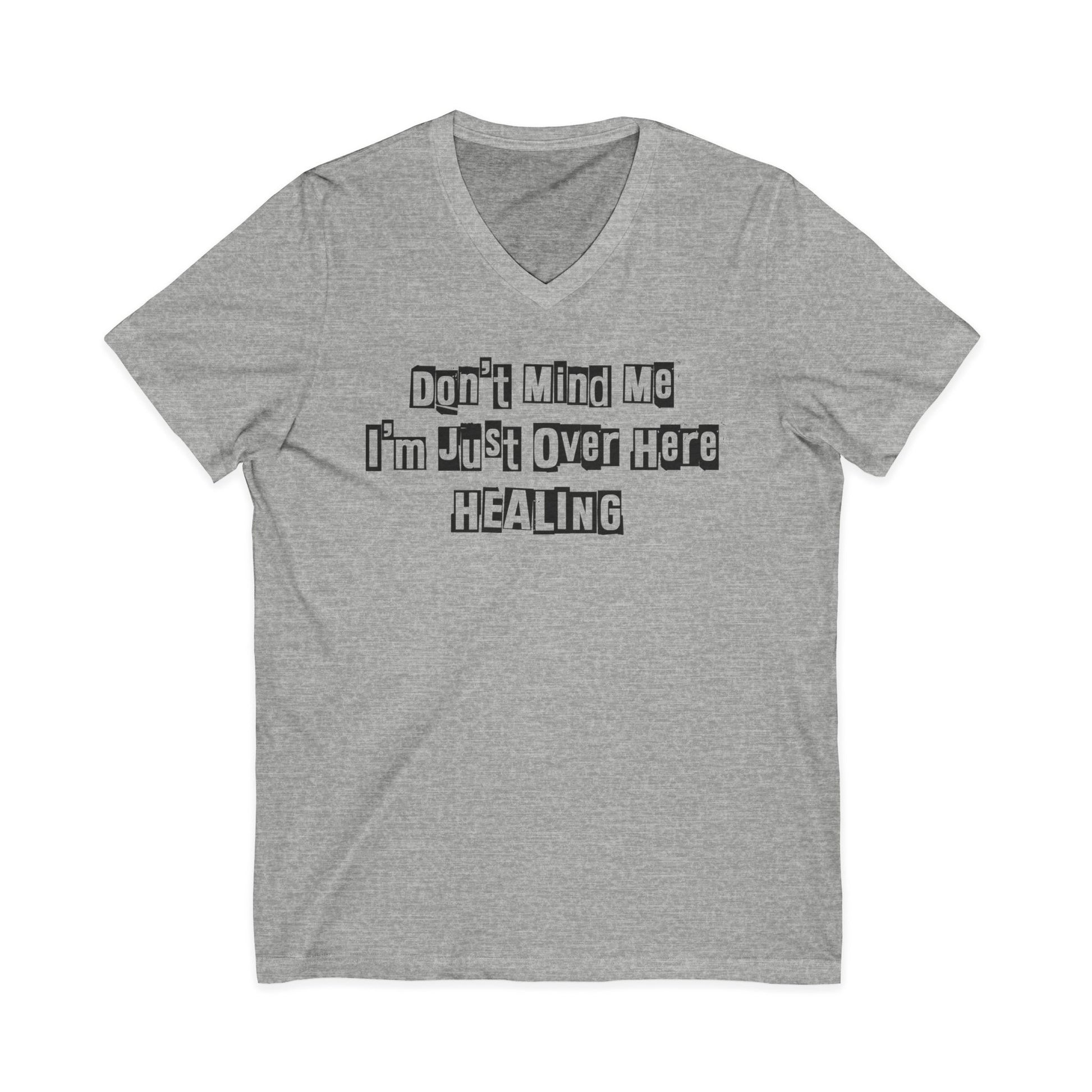 Heather grey JohnT V-neck T-shirt with the printed text “Don’t Mind Me I’m Just Over Here Healing” displayed flat on a plain background.