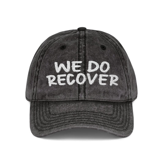Black distressed dad hat with bold white embroidered text reading We Do Recover, front view, Johny-T apparel