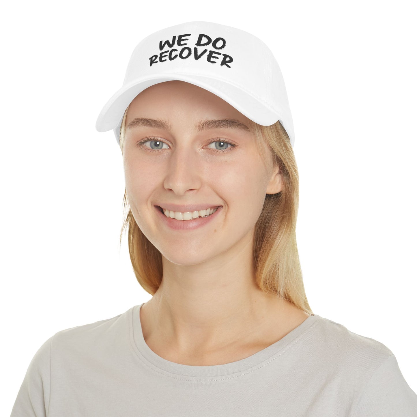 Smiling woman wearing a white low profile dad hat with printed We Do Recover text in a clean studio setting, Johny-T recovery apparel